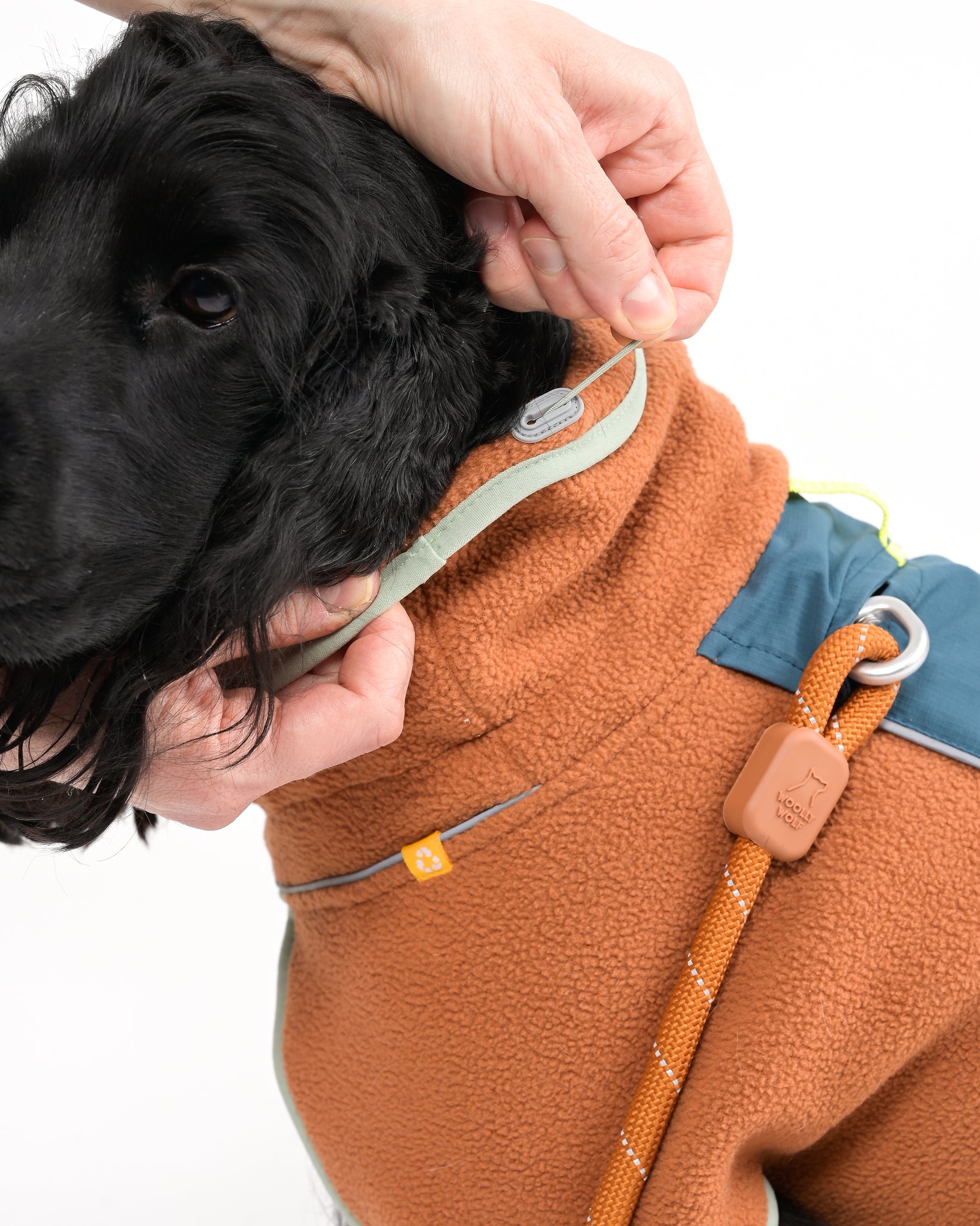 Dog wearing a brown fleece jacket , being adjusted by a person.