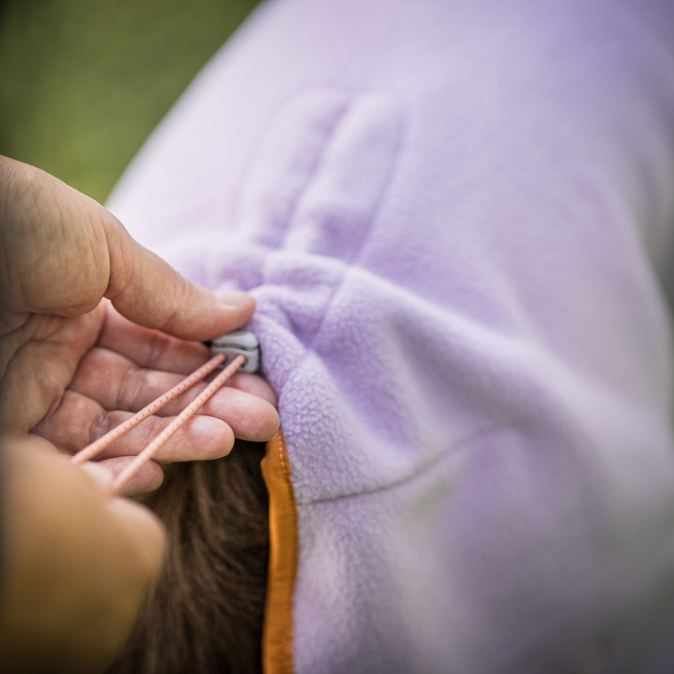 A person adjusting the drawstring on a purple fleece garment.