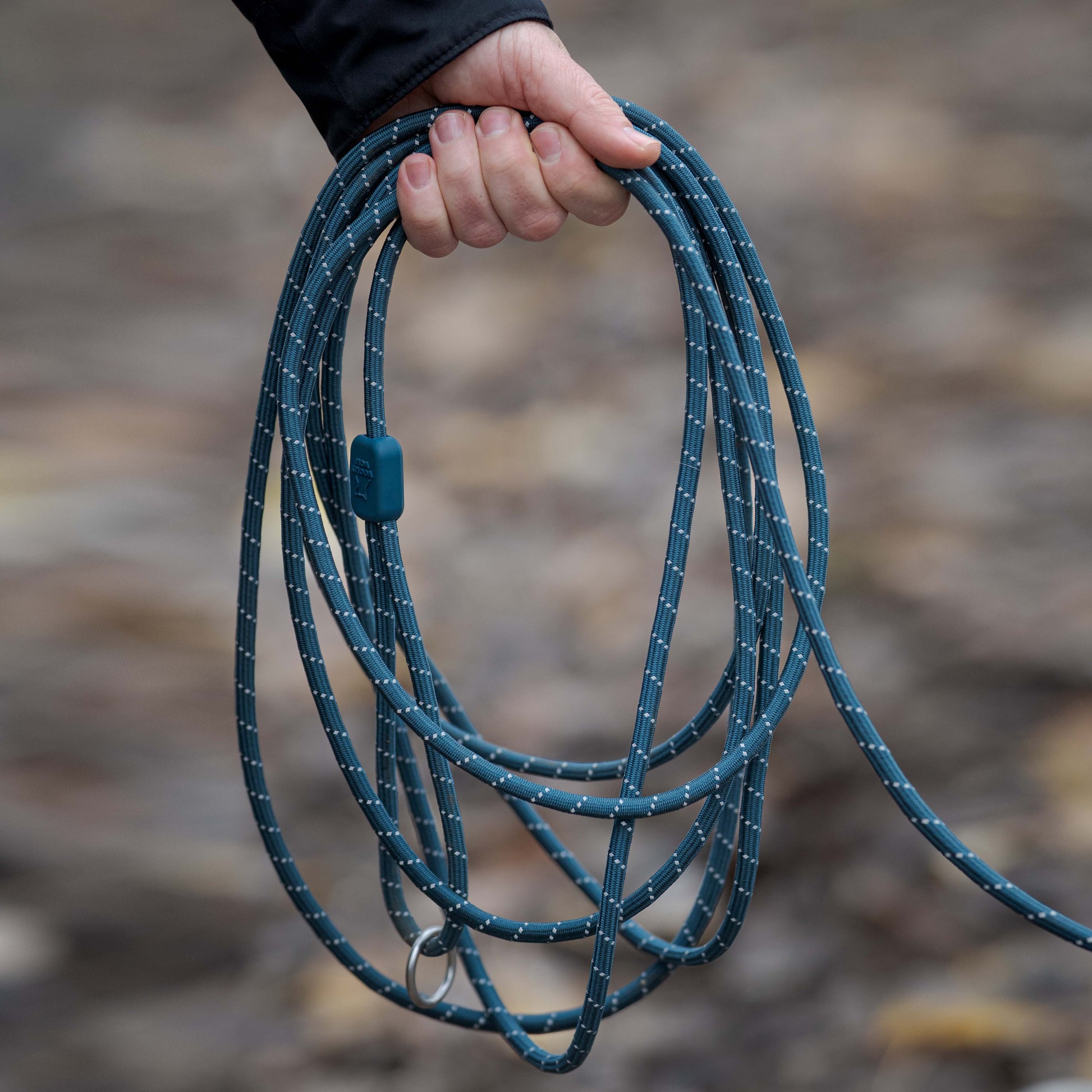 Hand holds coiled blue rope with white flecks and a metal ring.