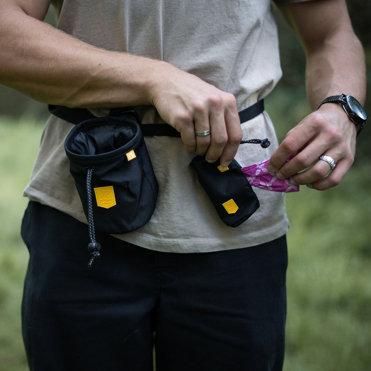 A person wearing a black waist bag and treat pouch, pulling a patterned bag from the smaller attachment.