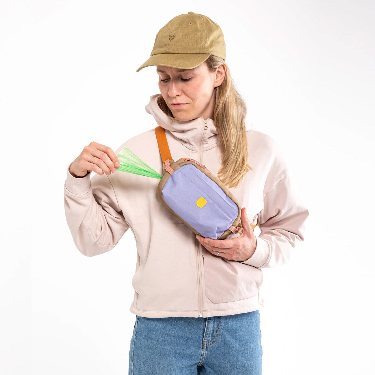 Woman in a tan hat pulls green dog waste bags from a purple and tan fanny pack.